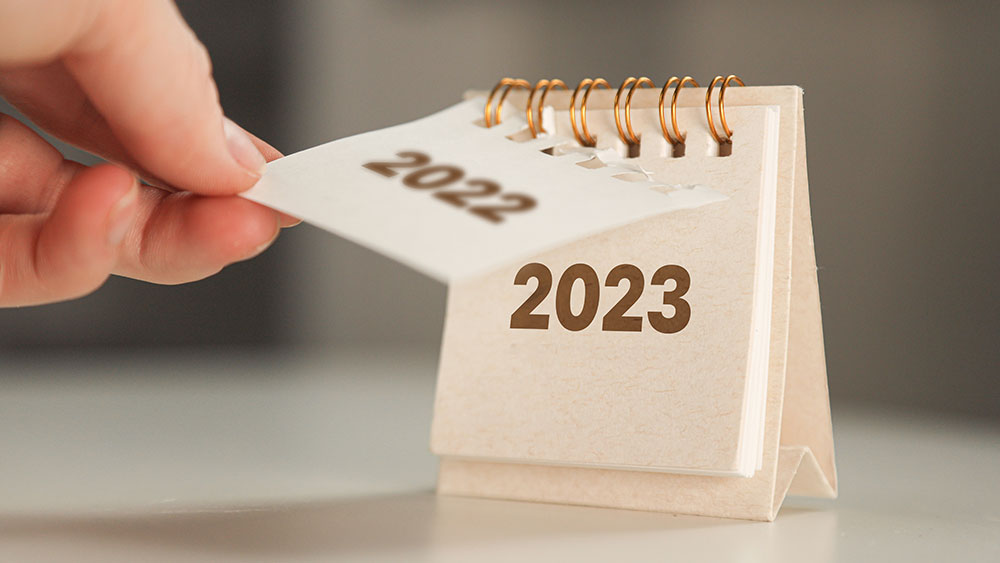 Kuvituskuva. Pöytäkalenterissa ihmisen käsi on kääntämässä vuoden 2022 lehteä vuoden 2023 edestä pois.