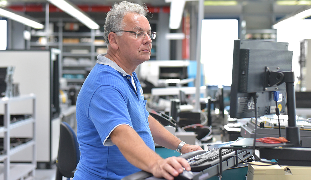 Kuvassa on harmaahiuksinen mies työkoneen ääressä tekemässä työtä.