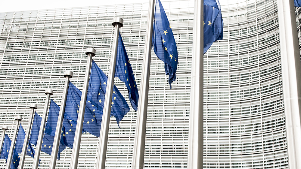 The image shows EU flags in front of the European Commission building.