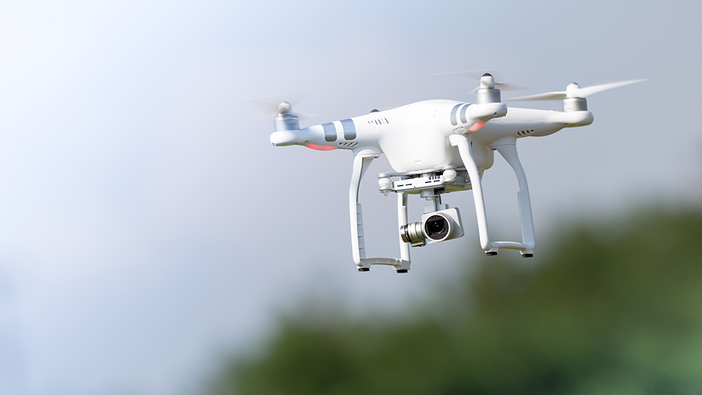 Kuvassa lentää vaalea nelikopteri eli drooni, jota voi käyttää myös tavaran kuljettamiseen