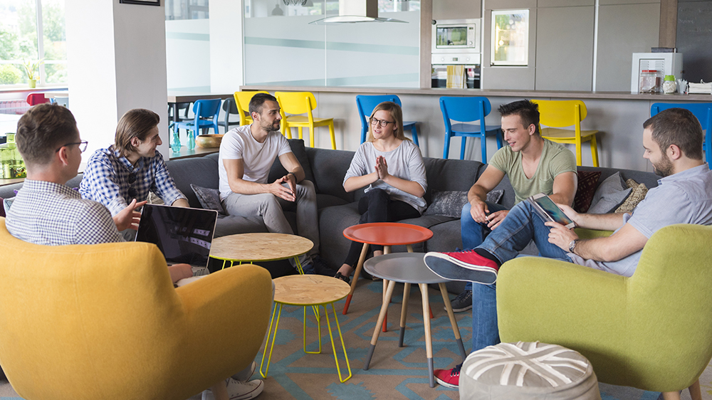 Kuvassa on ihmisiä, jotka istuvat kokouksessa vapaamuotoisesti puoliympyrässä.