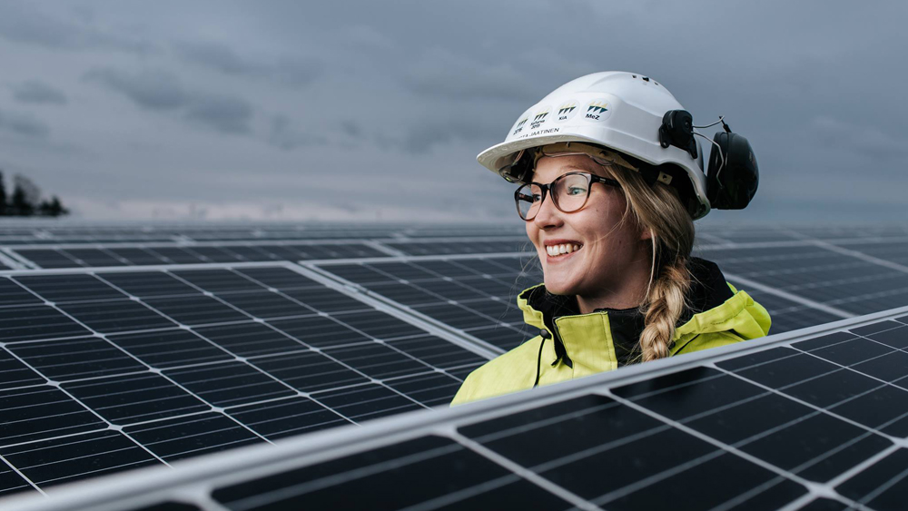 Kuvassa energia-alalla työskentelevä nainen aurinkopaneelien keskellä