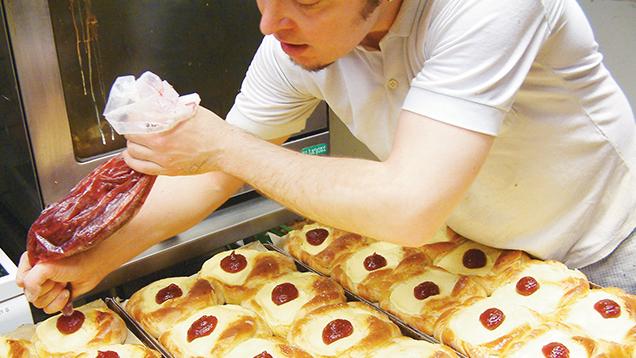 A man who works at a bakery makes sweet pastry.