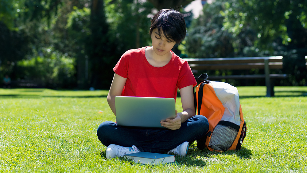 En ung invandrarkvinna med en laptop på gräsmattan.