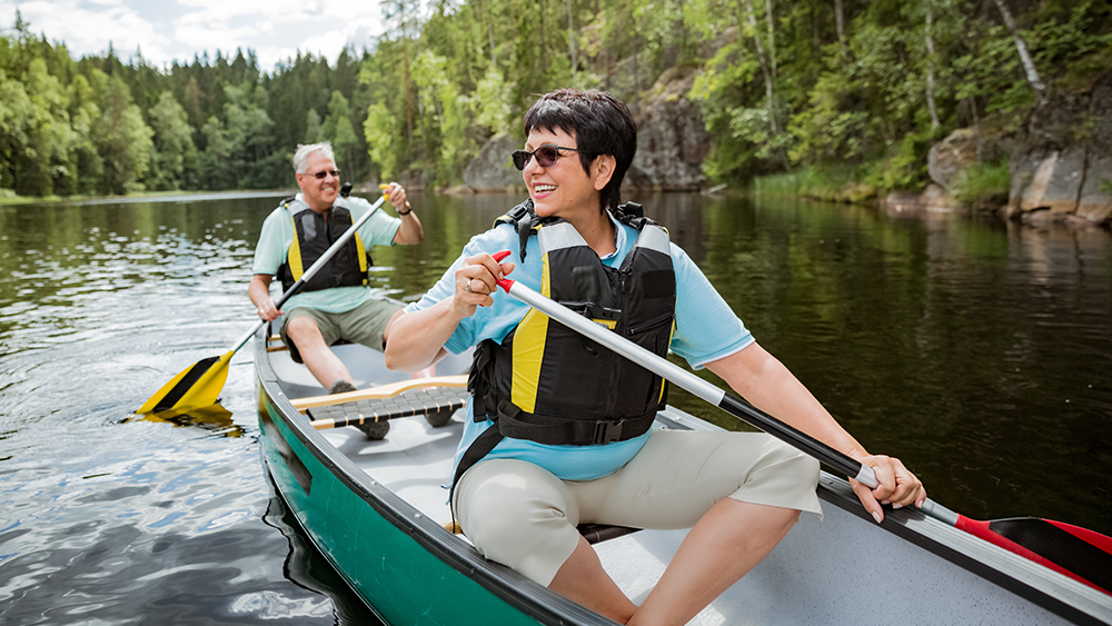 En man och en kvinna går med kanoten i finska natur.